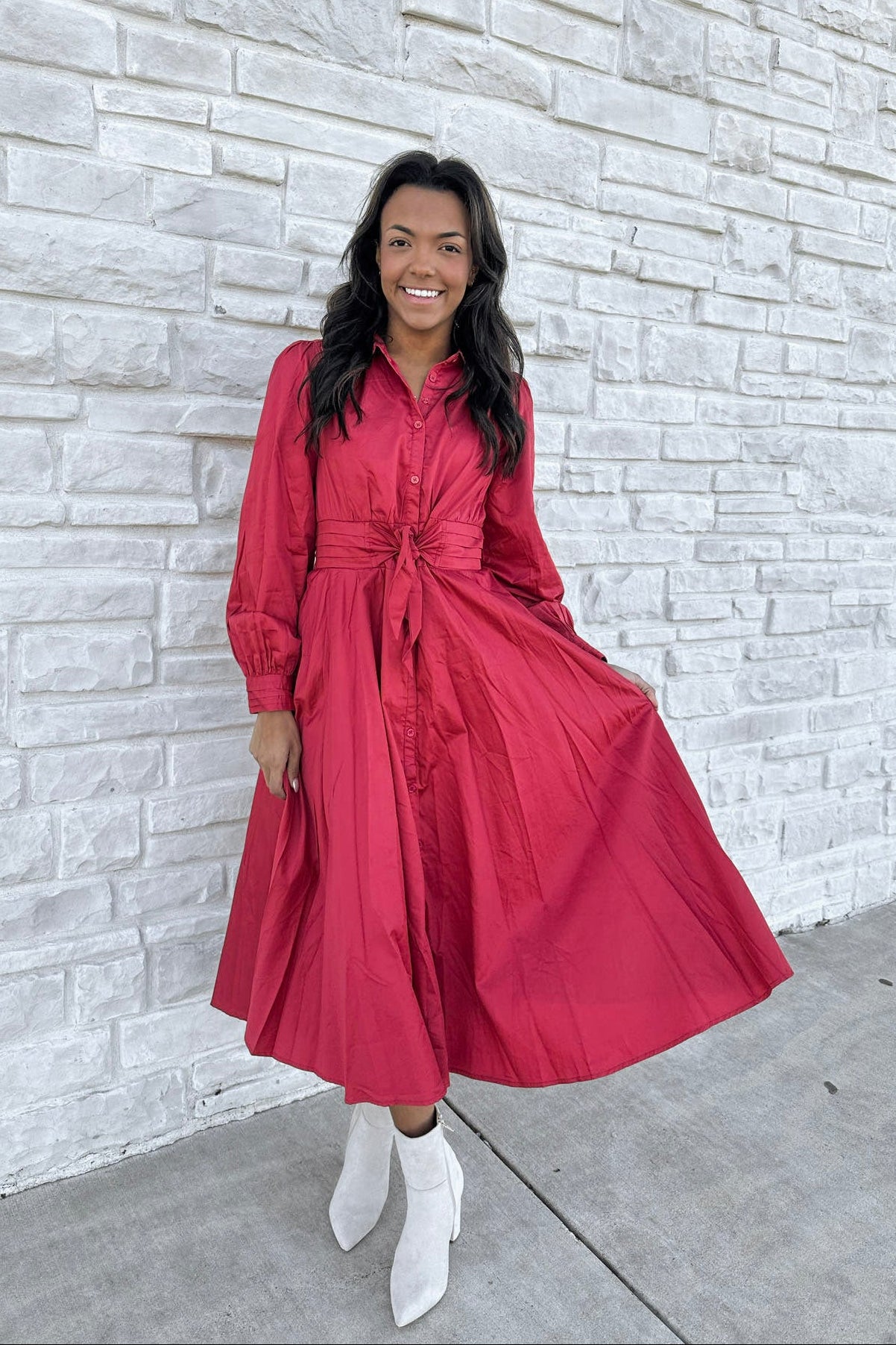 Woman in a red dress standing against a light stone wall.