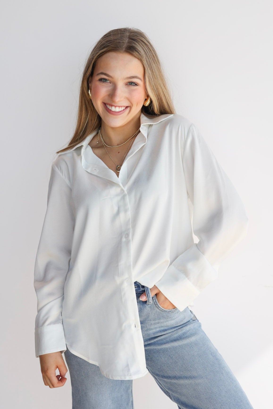 Woman wearing a white shirt and light blue jeans against a plain background