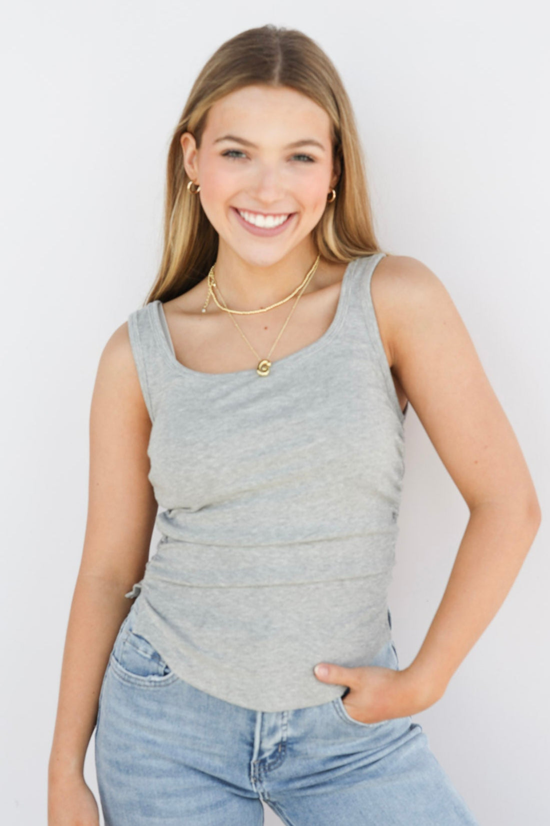 Woman wearing a gray tank top and light blue jeans against a white background