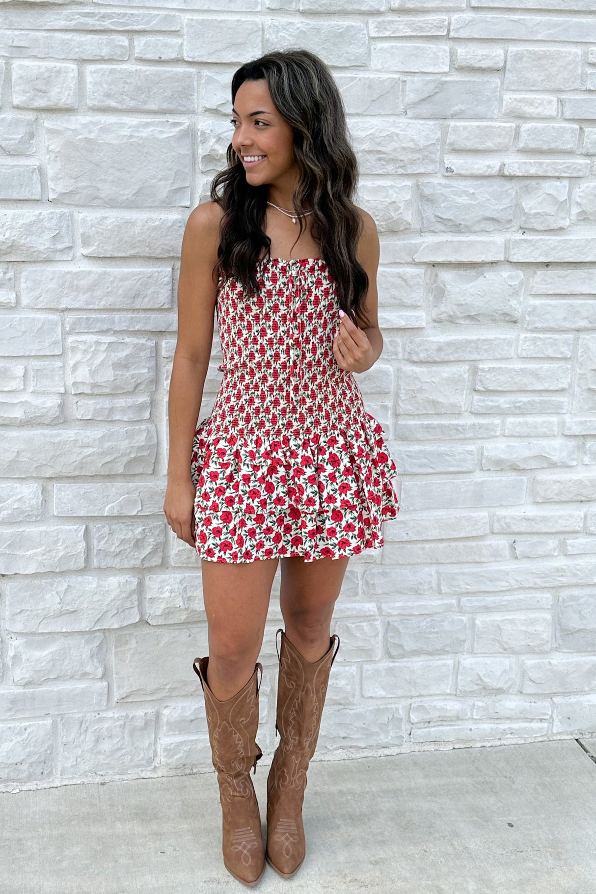 Woman wearing a red floral dress and brown boots against a light stone wall.