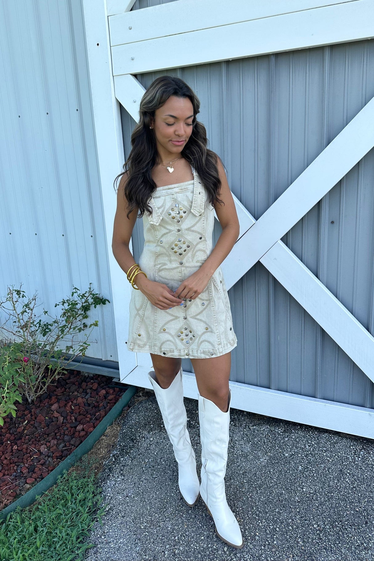 Woman in a white dress and knee-high boots standing against a white wooden gate.