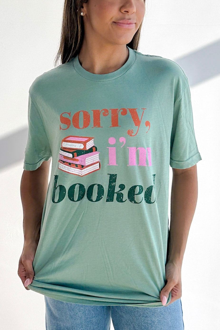 Woman wearing a green t-shirt with 'Sorry, I'm booked' text and book graphic.