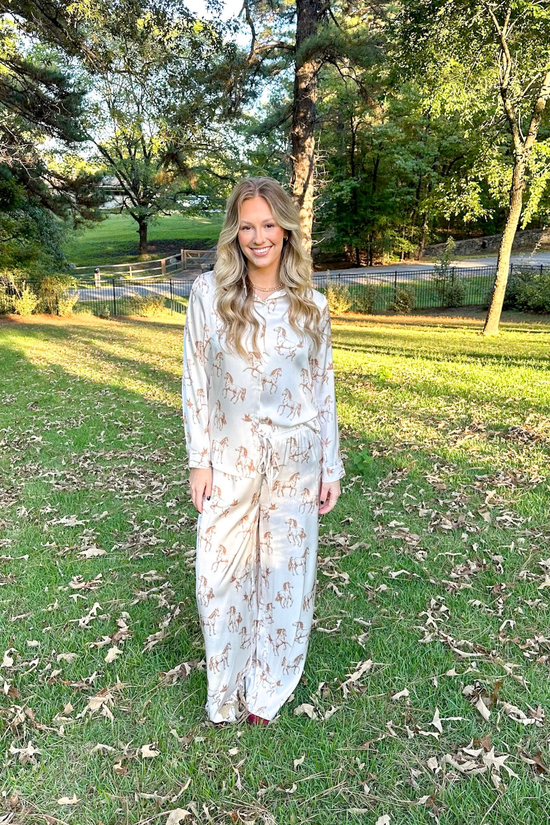 Woman in a floral dress standing in a park with trees and grass.