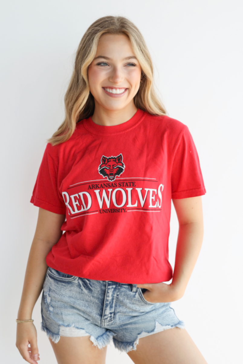 Person wearing a red 'Red Wolves' t-shirt with denim shorts on a white background