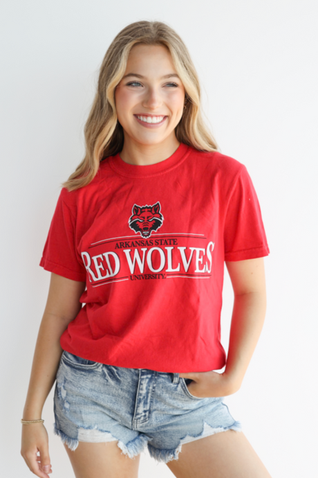 Person wearing a red 'Red Wolves' t-shirt with denim shorts on a white background
