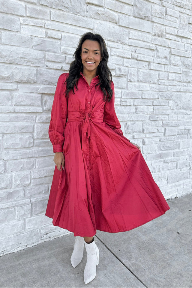 Woman in a red dress standing against a light stone wall.