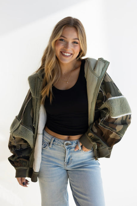 Woman wearing a green jacket over a black top and light blue jeans on a white background
