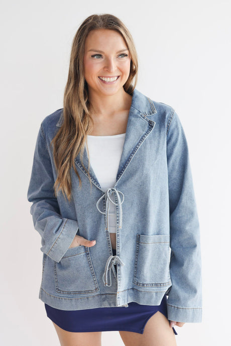 Woman wearing a light blue denim jacket over a white top and dark shorts on a white background