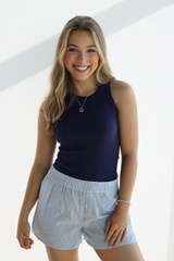 Woman wearing a navy tank top and light blue shorts on a white background