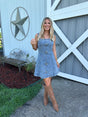 Woman in a blue dress with floral patterns standing in front of a white building with a star design.
