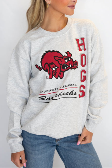 A female model wearing a gray sweatshirt with 'HOGS' and 'University of Arkansas' text on it.