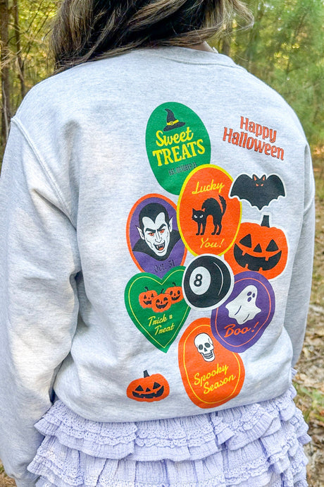 Person wearing a light gray sweatshirt with Halloween-themed graphics outdoors.