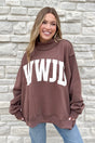 A smiling woman with long, light brown hair wears the WWJD/Amen Mockneck sweatshirt with bold white WWJD print, standing in front of a light stone wall. Her hands are in her pockets and she pairs it with blue jeans.