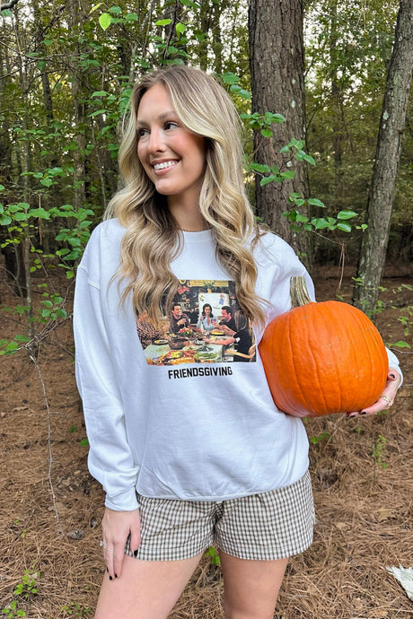 Woman in a forest holding a pumpkin wearing a 'Friendsgiving' shirt.