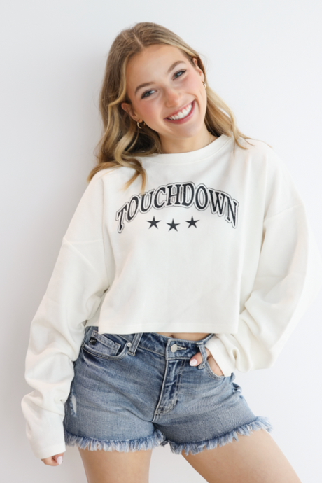 Woman wearing a white 'Touchdown' sweatshirt and denim shorts against a plain background