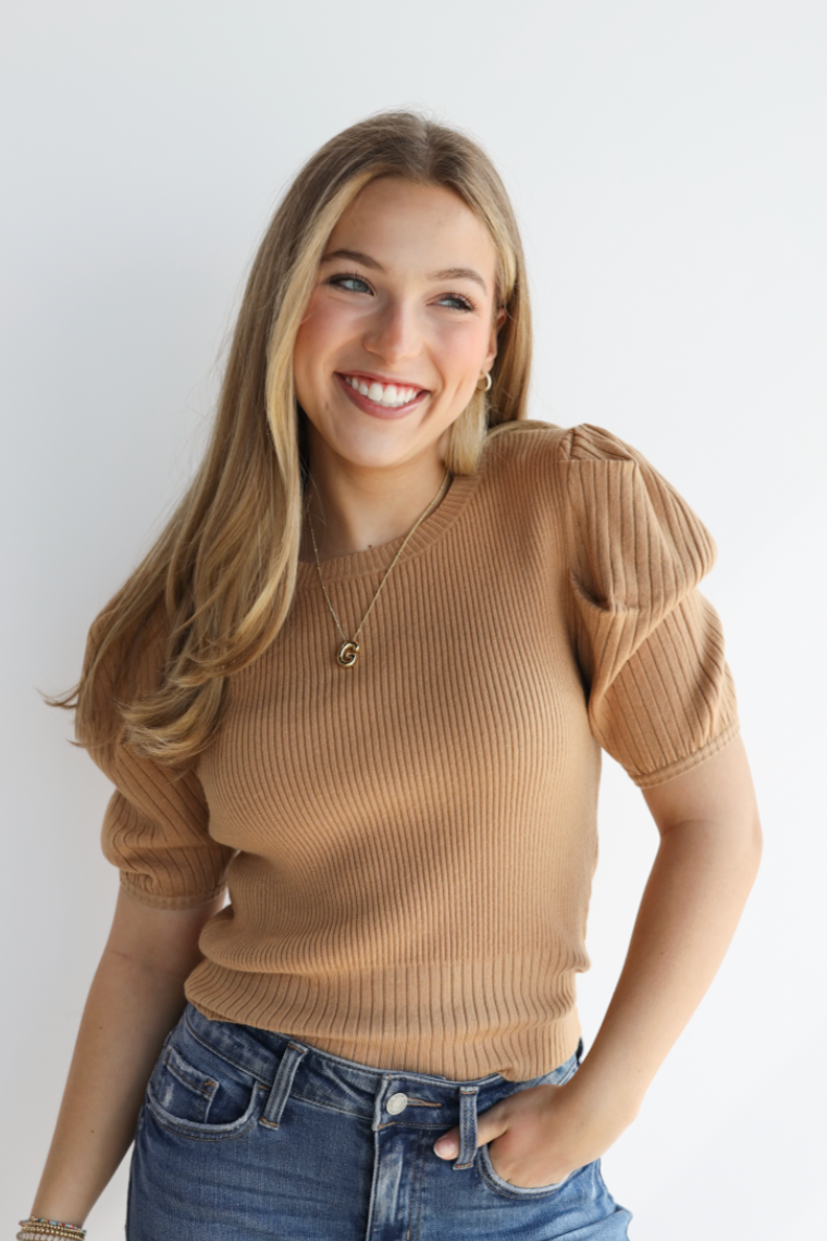 Woman wearing a brown sweater and blue jeans against a white background