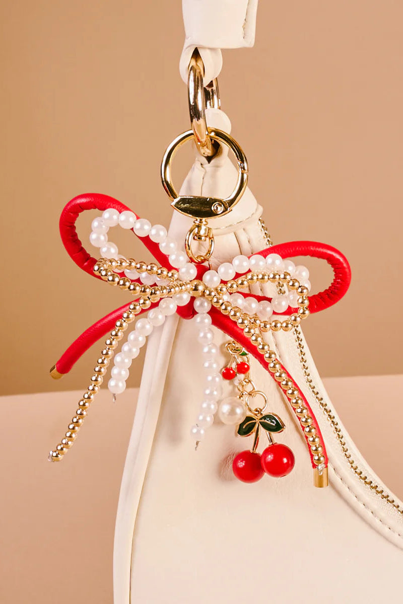 Decorative keychain with red bow, pearls, and cherries on a beige background